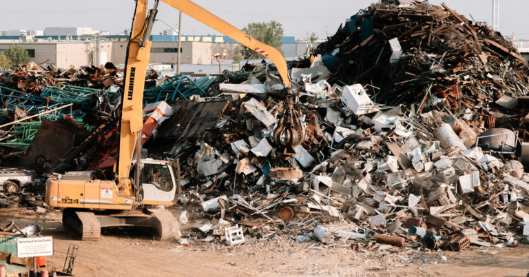 A crane sifts through a large pile of various recycled metals.